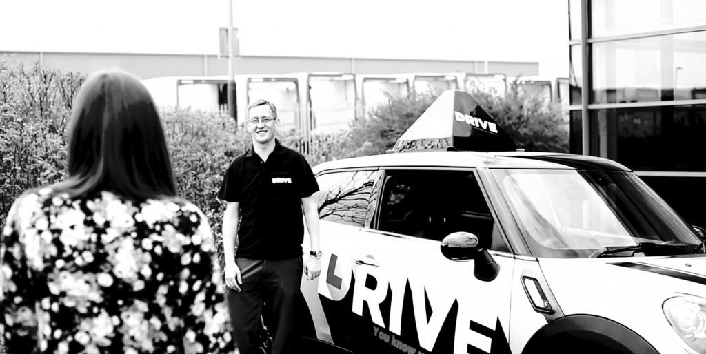driving instructor welcoming driving student in front of DRIVE instructor car